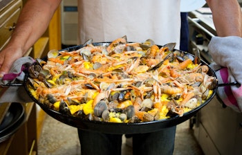 Kok bærer frisklavet skaldyrspaella fra et traditionelt baskisk gastronomisk selskab i San Sebastian, perfekt til madrejser i Spanien