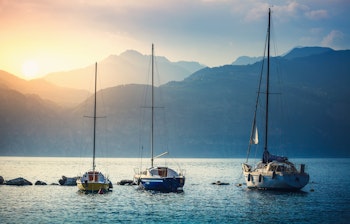 Sejlbåde på Gardasøen ved solnedgang med bjerge i baggrunden nær Malcesine i Italien