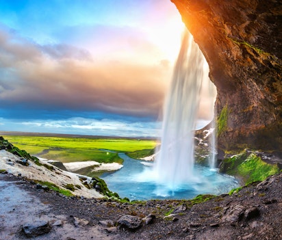 Betagende Seljalandsfoss vandfald badet i gyldent solnedgangslys med frodig grøn vegetation i det sydlige Island