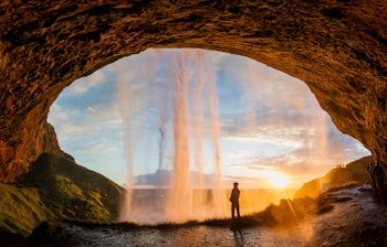 Person bag det ikoniske Seljalandsfoss vandfald ved solnedgang på Island, en unik naturoplevelse på vores rejse til Islands sydkyst