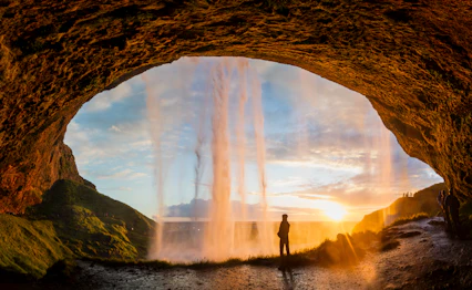 Person bag det ikoniske Seljalandsfoss vandfald ved solnedgang på Island, en unik naturoplevelse på vores rejse til Islands sydkyst