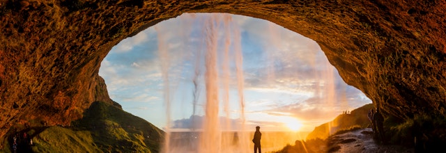 Person bag det ikoniske Seljalandsfoss vandfald ved solnedgang på Island, en unik naturoplevelse på vores rejse til Islands sydkyst