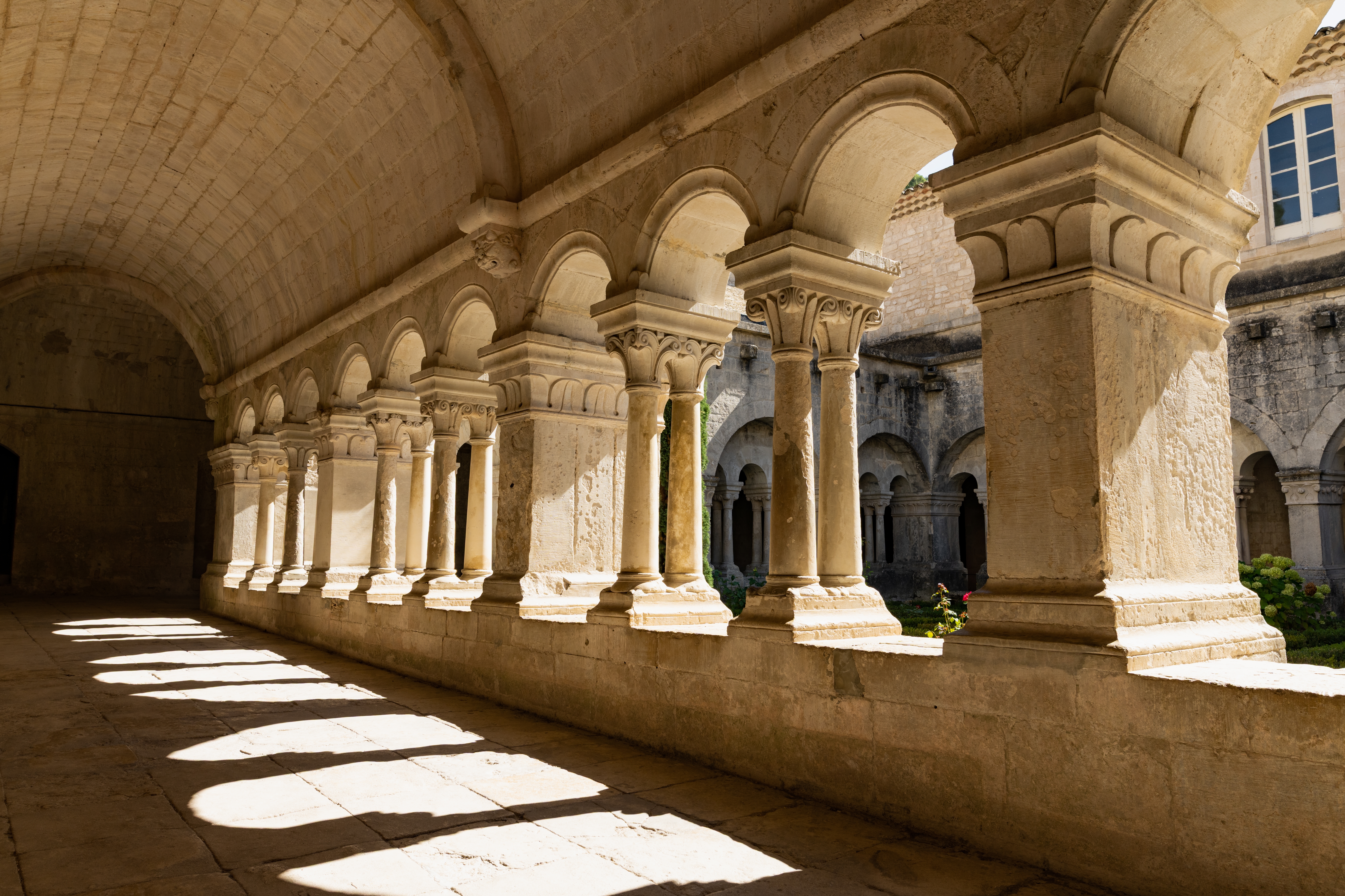 Solbeskinnede romanske buegange og udskårne søjler i den indre klostergård på Abbaye de Sénanque nær Gordes i Provence, Frankrig