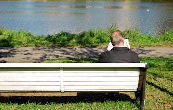 Ældre mand sidder afslappet på bænk og læser avis ved floden i efterårslandskab