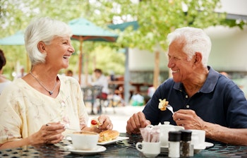 Ældre par smiler og nyder et måltid sammen på en udendørs café under deres ferie