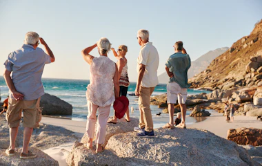 Gruppe af senior venner udforsker klippefyldt strand under ferie