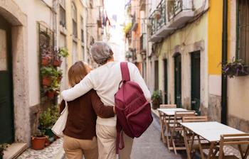Ældre par går arm i arm med rygsække på byvandring i Lissabon, perfekt til seniorferie i Portugal