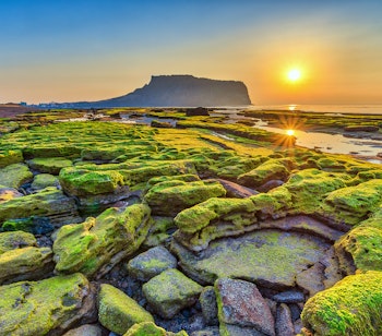 Betagende solopgang ved Seongsan Ilchulbong vulkankrater på Jeju-øen i Sydkorea, hvor det gyldne morgenlys oplyser dette UNESCO Verdensarvssted