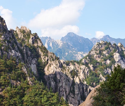 Vandrere nyder den imponerende udsigt fra granittoppen af Seoraksan-bjerget i Sydkorea, omgivet af dramatiske klippeformationer og skovklædte bjerge