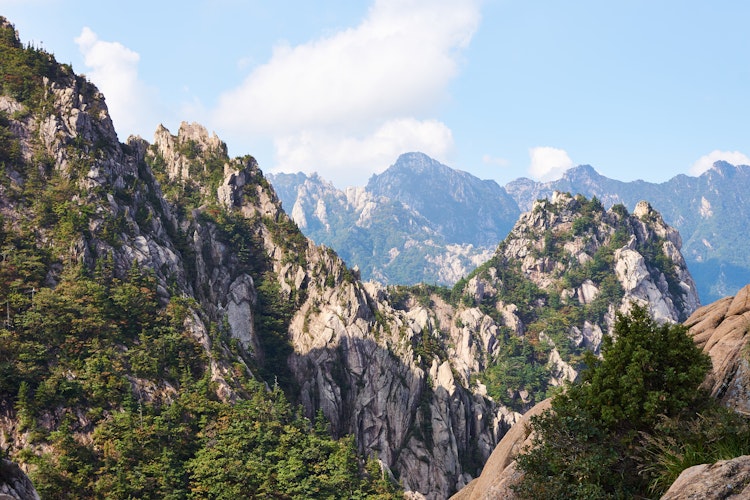 Vandrere nyder den imponerende udsigt fra granittoppen af Seoraksan-bjerget i Sydkorea, omgivet af dramatiske klippeformationer og skovklædte bjerge