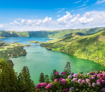 Panoramaudsigt over de ikoniske tvillingesøer i Sete Cidades med blåt og grønt vand, omgivet af frodige bjerge og lilla hortensiaer, set fra Vista do Rei udsigtspunktet på São Miguel, Azorerne