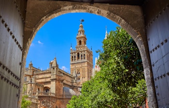 Udsigt til Sevilla Katedrals ikoniske Giralda-tårn indrammet af en smuk buet døråbning i Alcazar-paladset - historiske arkitektoniske landemærker i Andalusien, Spanien