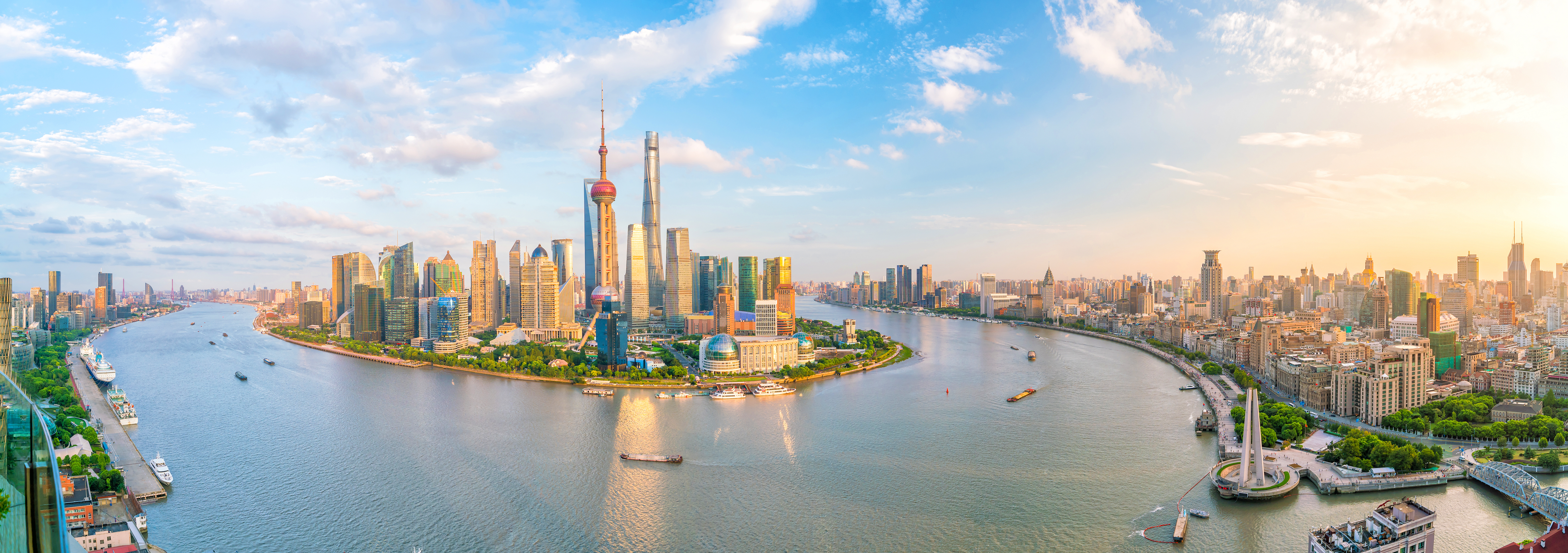 Imponerende udsigt over Shanghais moderne skyline med Pudong finansdistriktets karakteristiske skyskrabere og Oriental Pearl Tower, der spejler sig i Huangpu-floden under en klar blå himmel