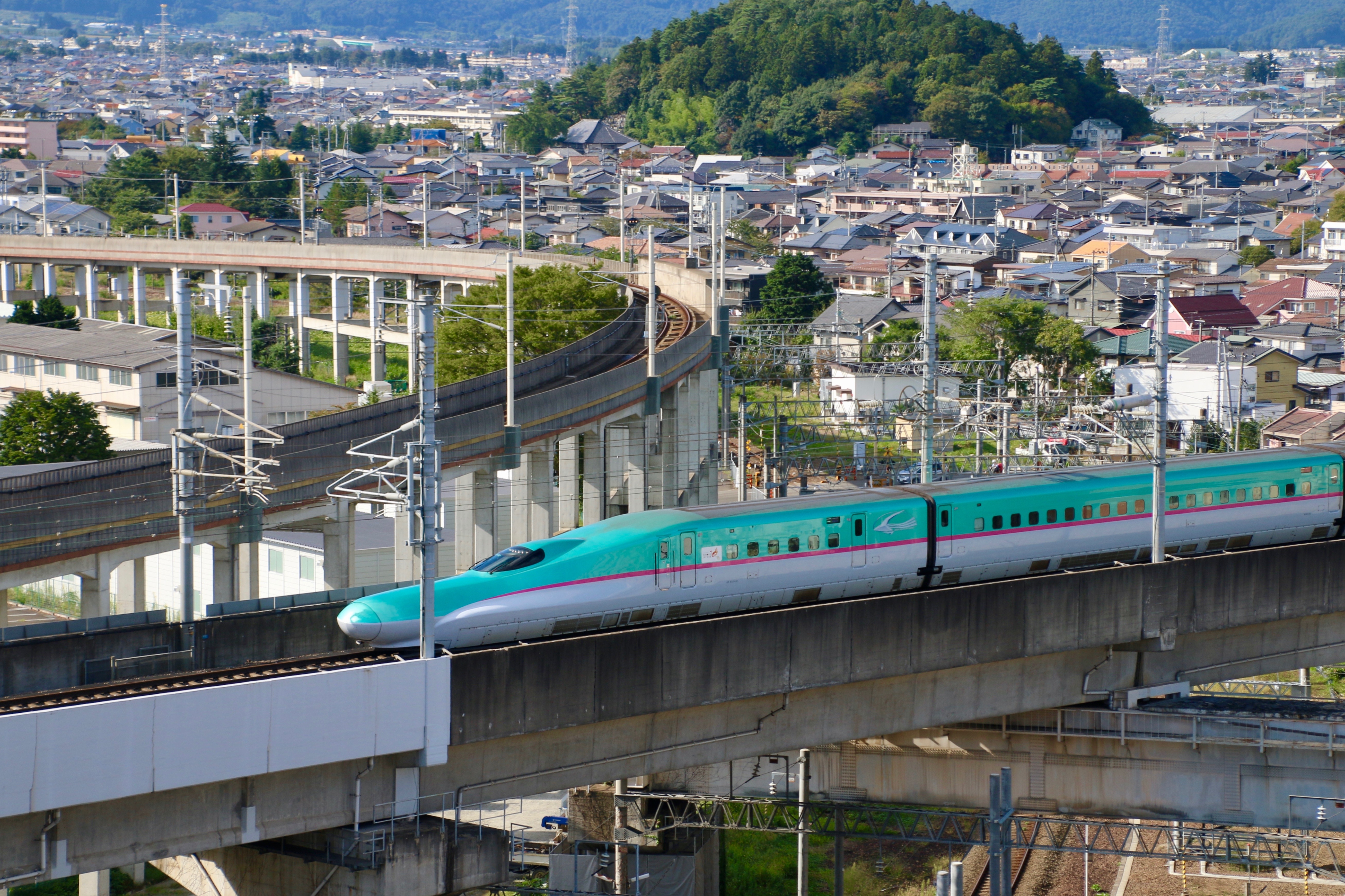 Japansk Shinkansen højhastighedstog kører gennem Fukushima by med bjerge i baggrunden