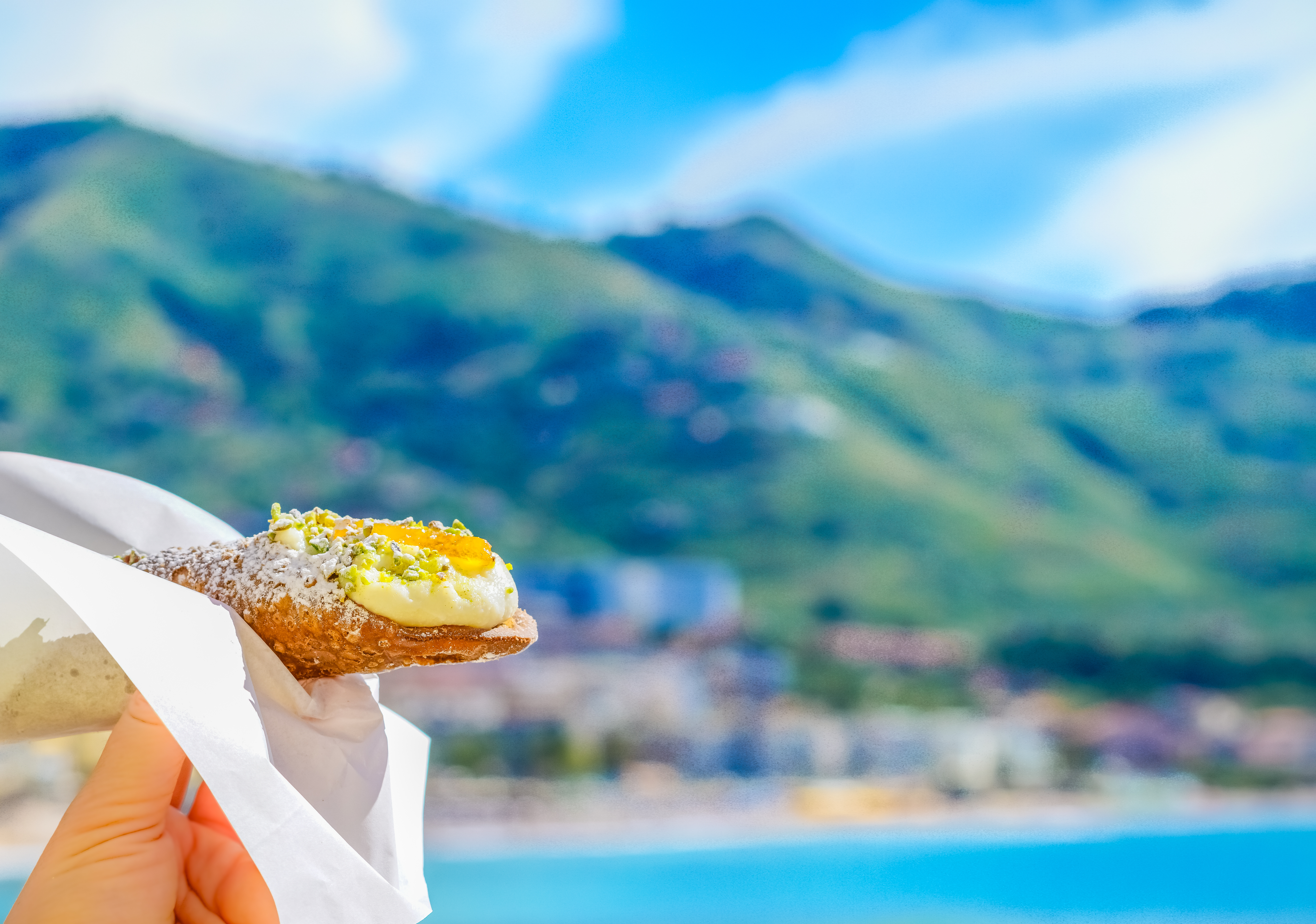 Traditionelle sicilianske cannoli fyldt med sød ricottaost, fotograferet med Middelhavets blå vand som baggrund på Sicilien
