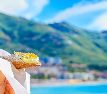 Traditionelle sicilianske cannoli fyldt med sød ricottaost, fotograferet med Middelhavets blå vand som baggrund på Sicilien
