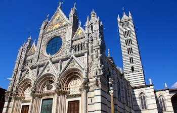 Siena Domkirke med imponerende gotisk facade, stribede marmormønstre og klokketårn under blå himmel i Toscana
