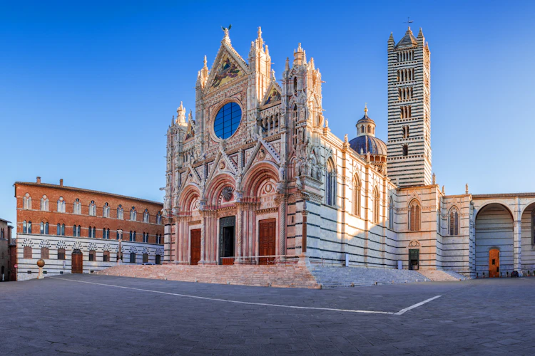 Panoramaudsigt over Sienas smukke domkirke Duomo di Siena med gotisk facade og stribet klokketårn i solopgang, Toscana, Italien