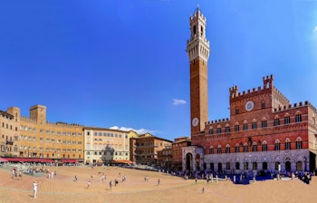 Panoramaudsigt over den berømte Piazza del Campo i Siena med det historiske Palazzo Pubblico og Torre del Mangia tårnet under en klar blå himmel