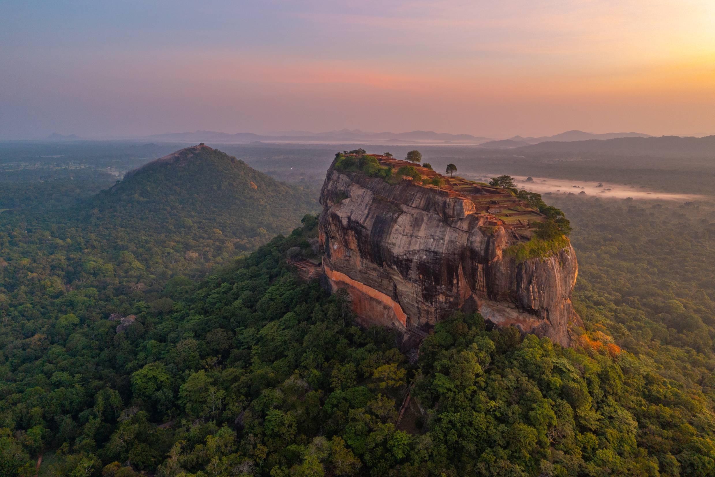 Betagende luftfoto af Sigiriya klippefæstning ved solopgang omgivet af frodig jungle i Sri Lanka, et UNESCO verdensarvssted