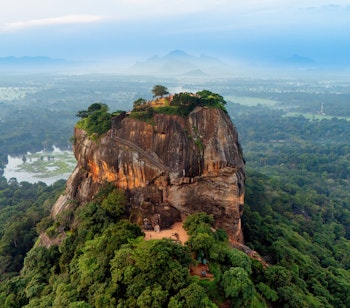 Sigiriya klippeborgen i morgenlys omgivet af frodig grøn vegetation og dis i Sri Lanka, et UNESCO verdensarvsted