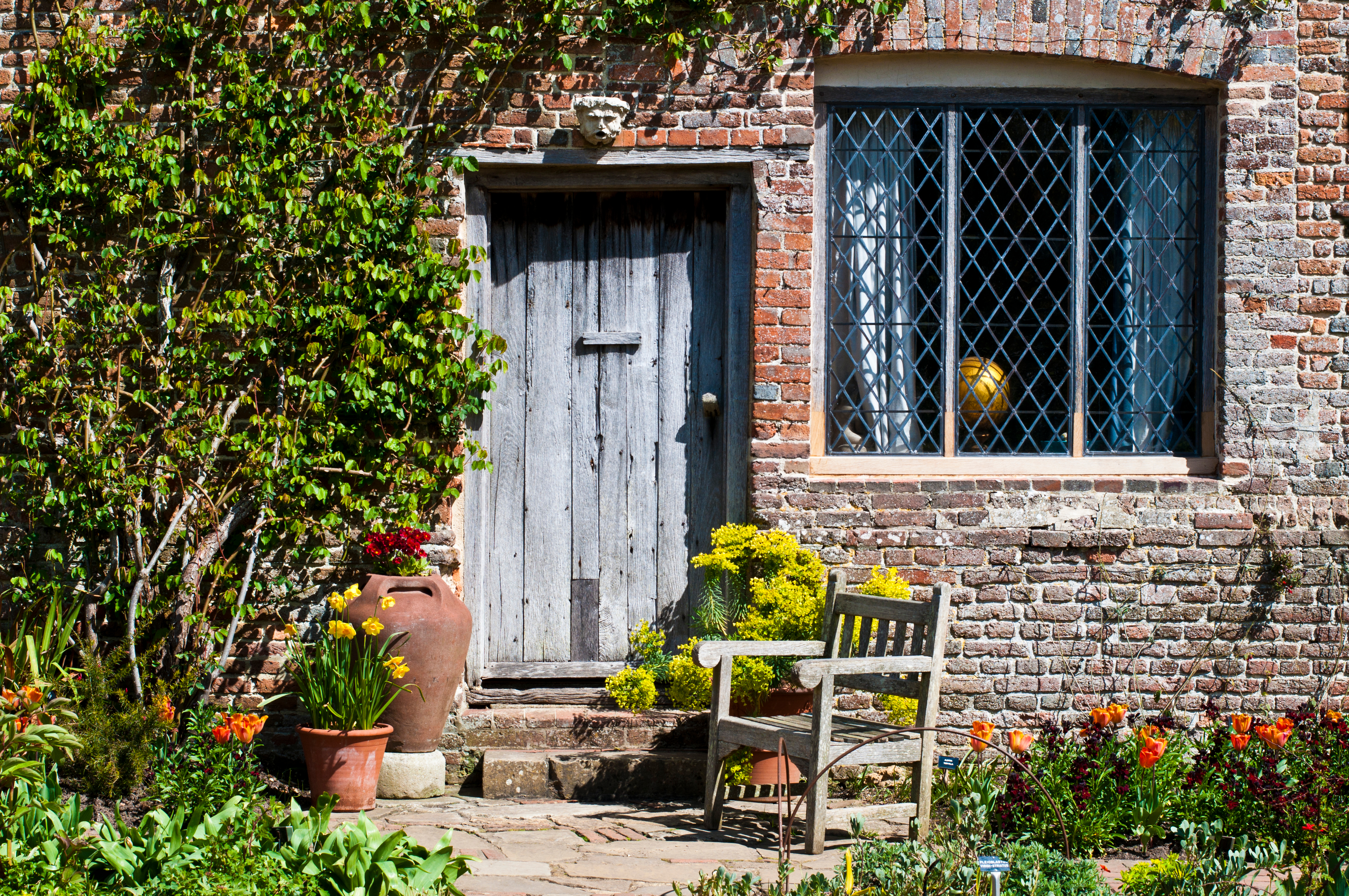 Charmerende historisk cottage facade ved Sissinghurst Gardens i Kent, England, med en gammel træddør, rudevindue og farverige forårsblomster