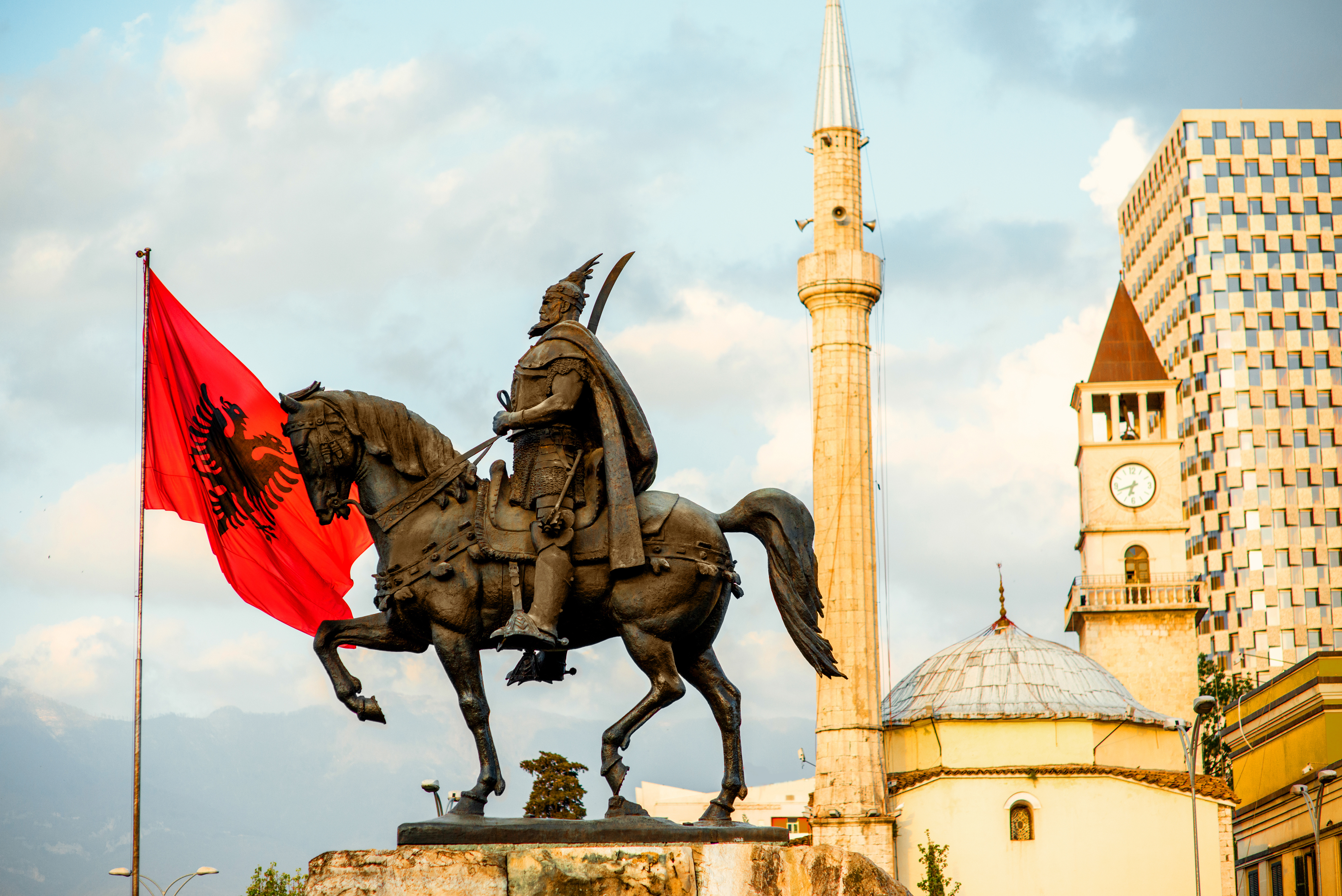 Skanderbeg monumentet med det albanske flag i Tiranas centrum, med Et'hem Bey moskeen og klokketårnet i baggrunden