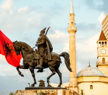 Skanderbeg monumentet med det albanske flag i Tiranas centrum, med Et'hem Bey moskeen og klokketårnet i baggrunden