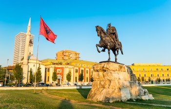 Skanderbeg-pladsen i Tirana med det berømte ryttermonument, det albanske flag og den historiske Et'hem Bey-moske under en klar blå himmel