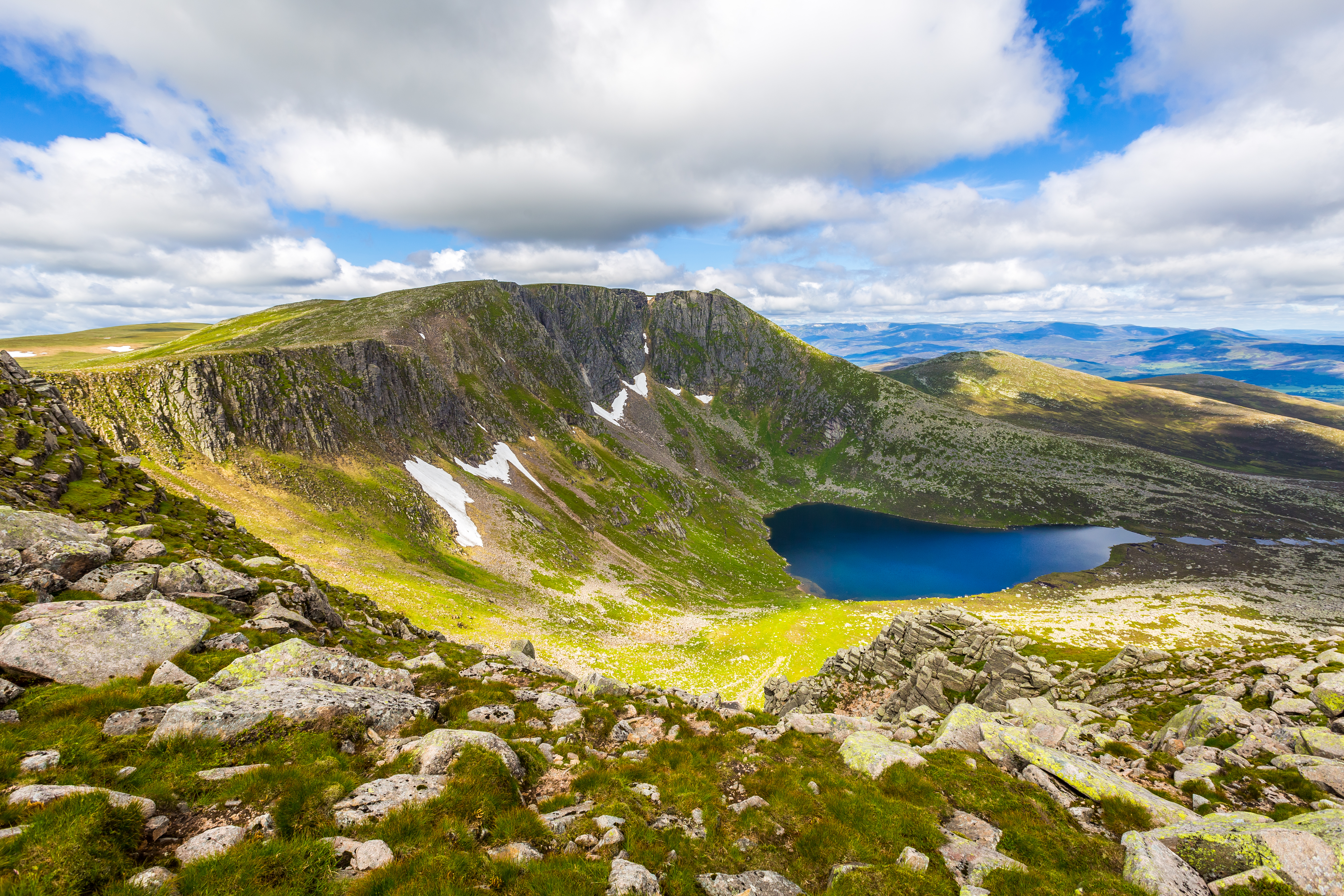 Smuk højlandssø omgivet af dramatiske klipper og grønne bjerge i Skotlands Cairngorms Nationalpark