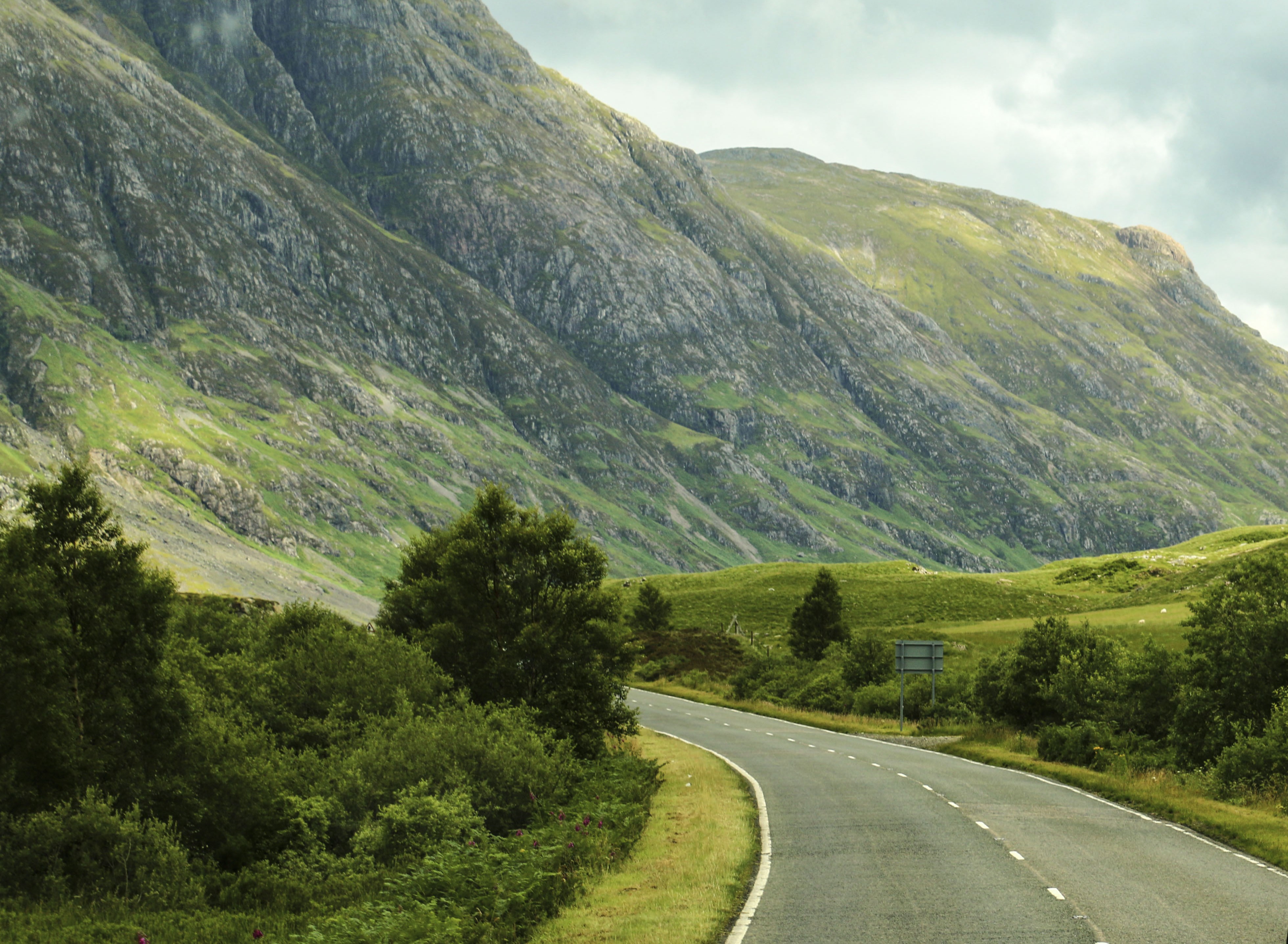 Malerisk bjergvej gennem skotske højland med bil kørende gennem grøn dal