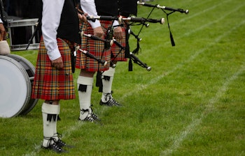Traditionelt skotsk sækkepibeorkester i røde tartan-kilte og formelle dragter, opstillet på den grønne bane ved Highland Games i Crieff, der viser den autentiske skotske kulturarv.