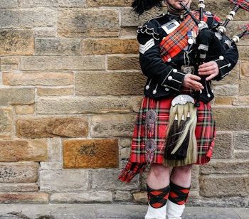 Traditionel skotsk sækkepiber i rød og sort kilt optræder ved Edinburghs historiske stenmur