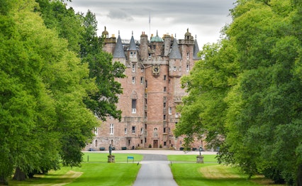 Historisk skotsk slot med røde sandstenmure omgivet af frodige grønne træer og velplejet park