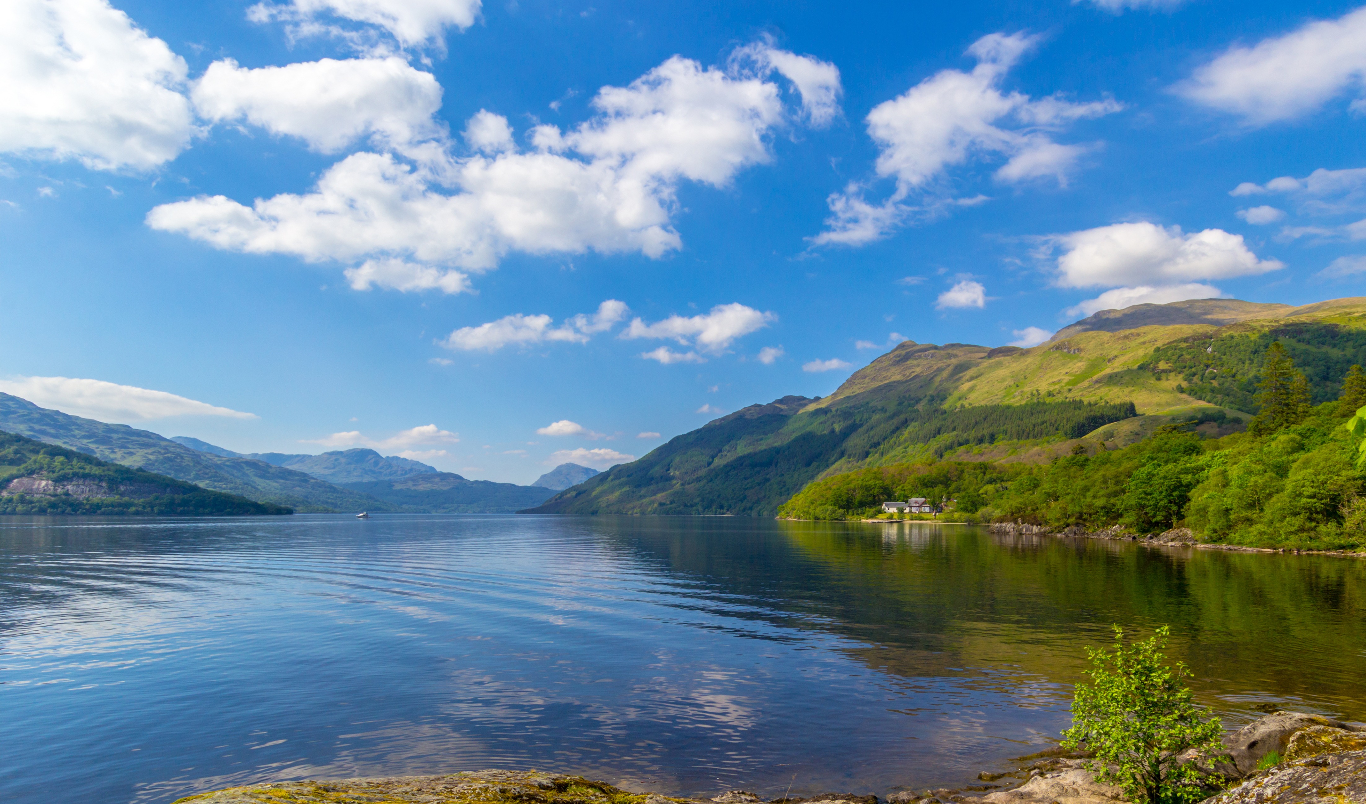Smukt skotsk sølandskab med grønne bjerge og stille blåt vand i sommerlys