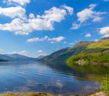Smukt skotsk sølandskab med grønne bjerge og stille blåt vand i sommerlys