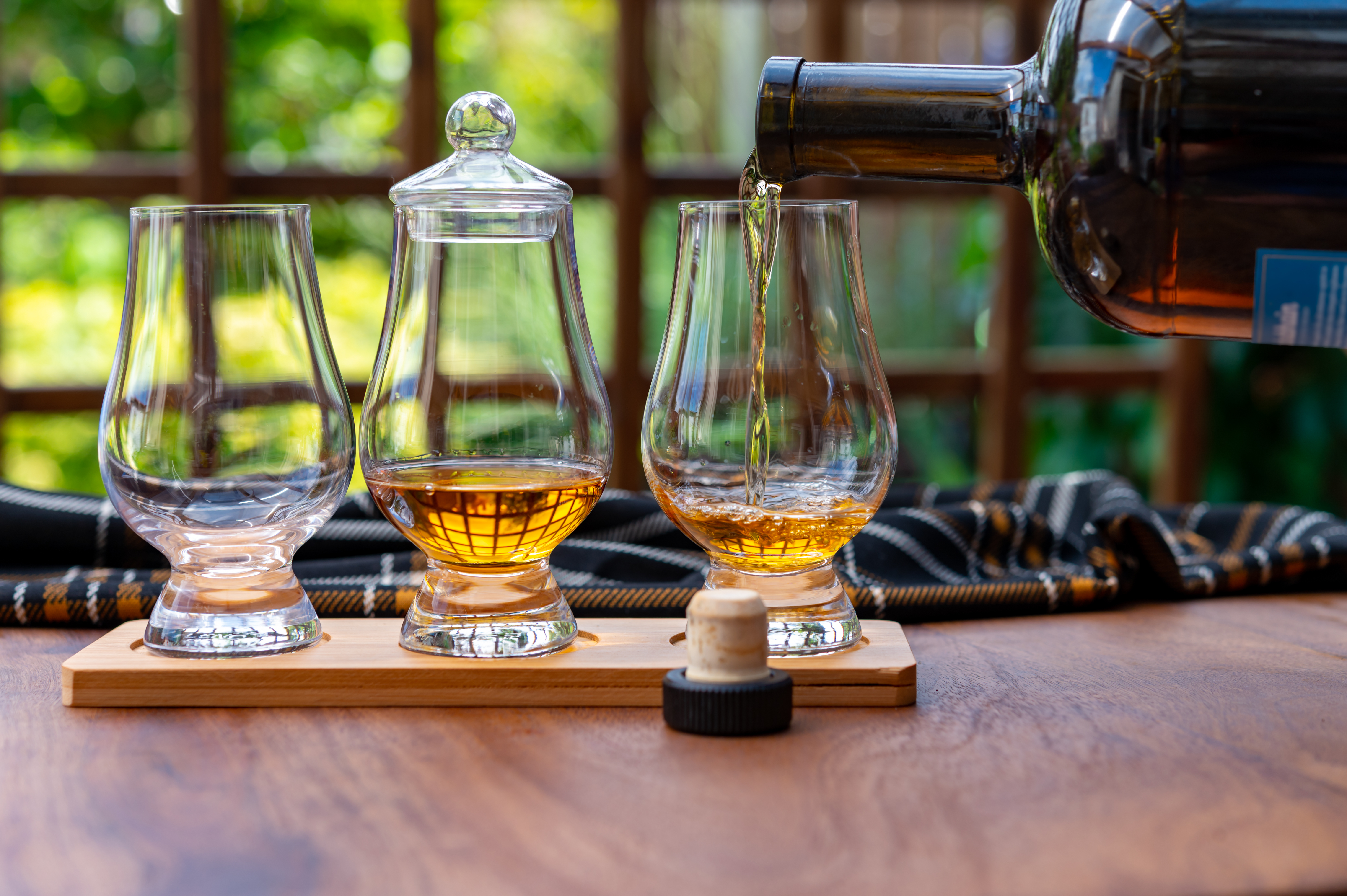 Forskellige gyldne skotske whiskyer serveret til smagning i smukke glas ved et trævindue i et traditionelt skotsk hus