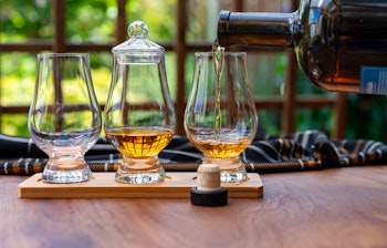 Forskellige gyldne skotske whiskyer serveret til smagning i smukke glas ved et trævindue i et traditionelt skotsk hus