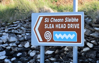 Vejskilt ved den maleriske Slea Head Drive turistrute på Dingle-halvøen i Irland med Atlanterhavet og grønne bakker i baggrunden