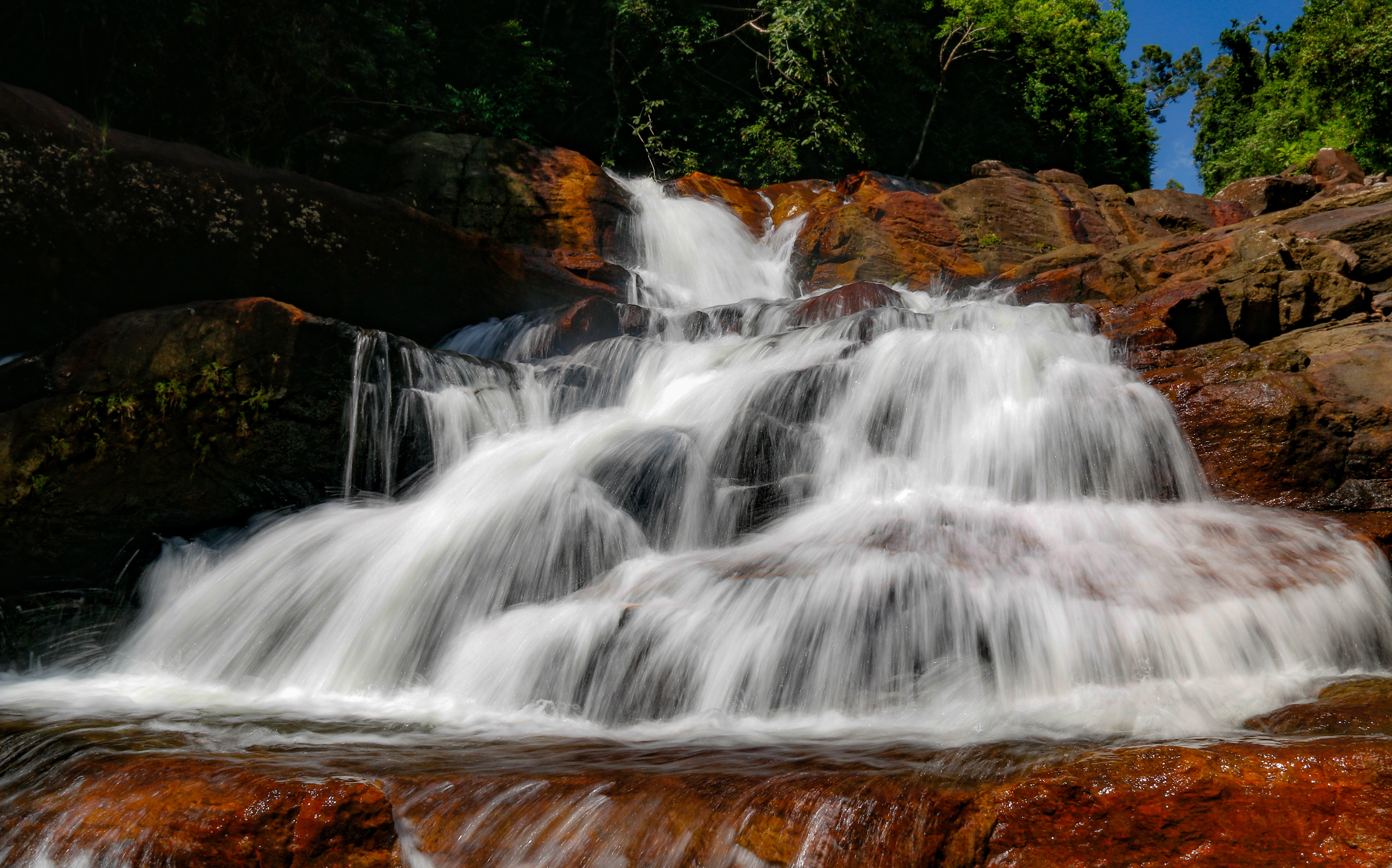 Smuk vandfald der styrter ned over røde sandstensklipper omgivet af grøn skov