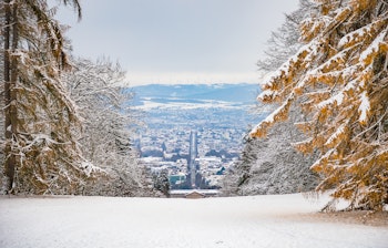 Snedækkede træer og byudsigt gennem vinterlandskab med bjerge i baggrunden