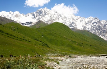 Majestætiske snedækkede bjergtinder over frodige grønne dale i Kaukasus bjergene i Georgien, perfekt til vandreferie om sommeren