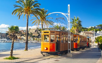 Den ikoniske orange sporvogn der kører mellem Soller og Port de Soller på Mallorca med smuk udsigt over Middelhavet og palmer langs den historiske rute