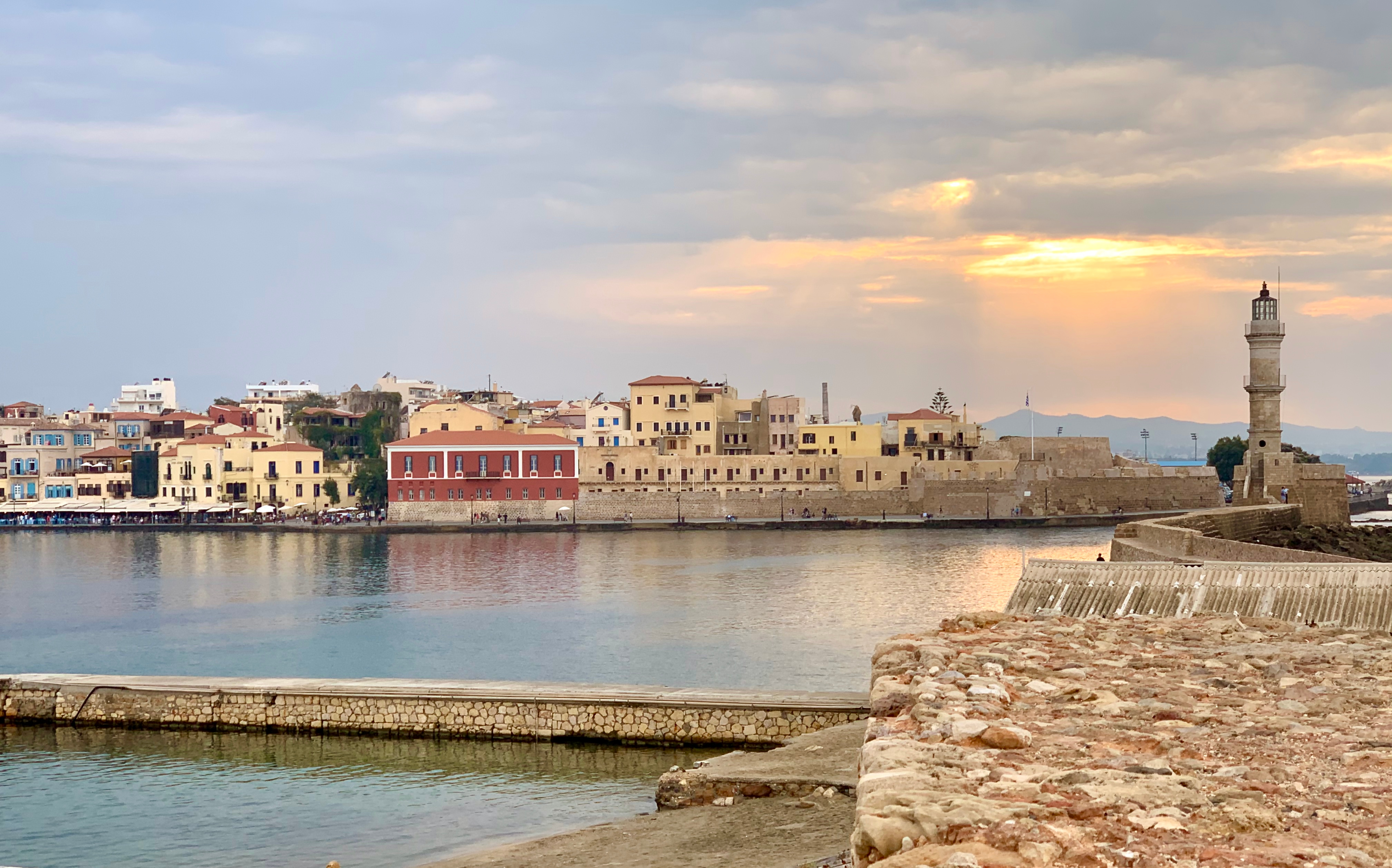 Malerisk solnedgang over Chania havn med brolagte stier der fører til det ikoniske fyrtårn på Kretas kyst