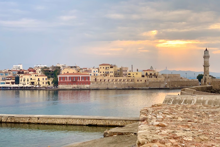 Malerisk solnedgang over Chania havn med brolagte stier der fører til det ikoniske fyrtårn på Kretas kyst