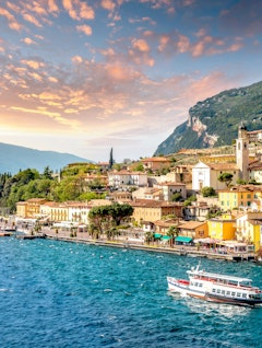 Idyllisk panoramaudsigt over Limone sul Garda med farverige bygninger ved Gardasøens blå vand og majestætiske bjerge i solnedgangslys