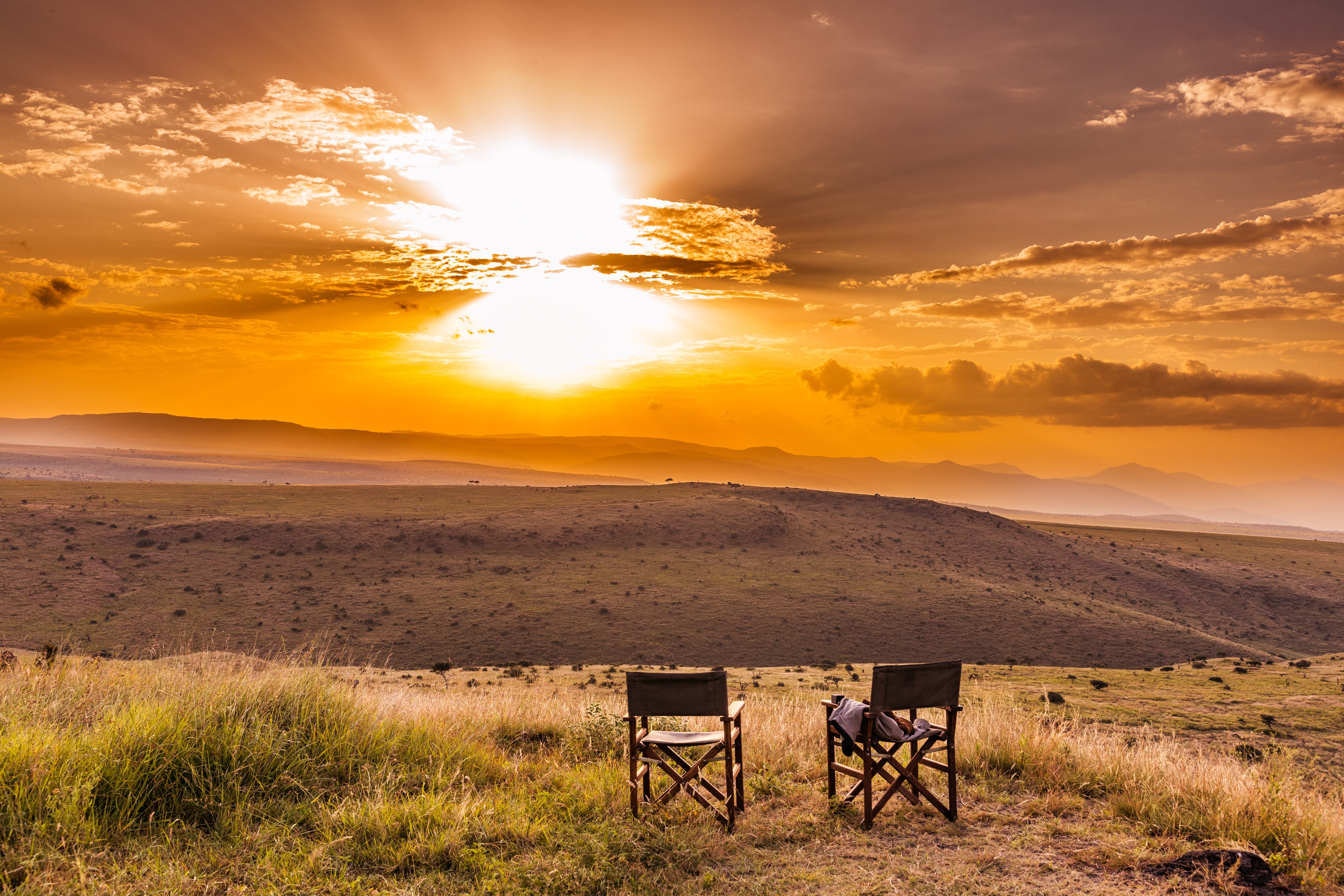 To campingstole med udsigt over den gyldne savanne ved solnedgang i Lewa Wildlife Conservancy, Kenya. Perfekt til safarioplevelser.