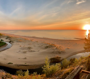 Betagende solnedgang over sandstranden i Saulkrasti ved Østersøen i Letland med gyldent sollys over kystlinjen