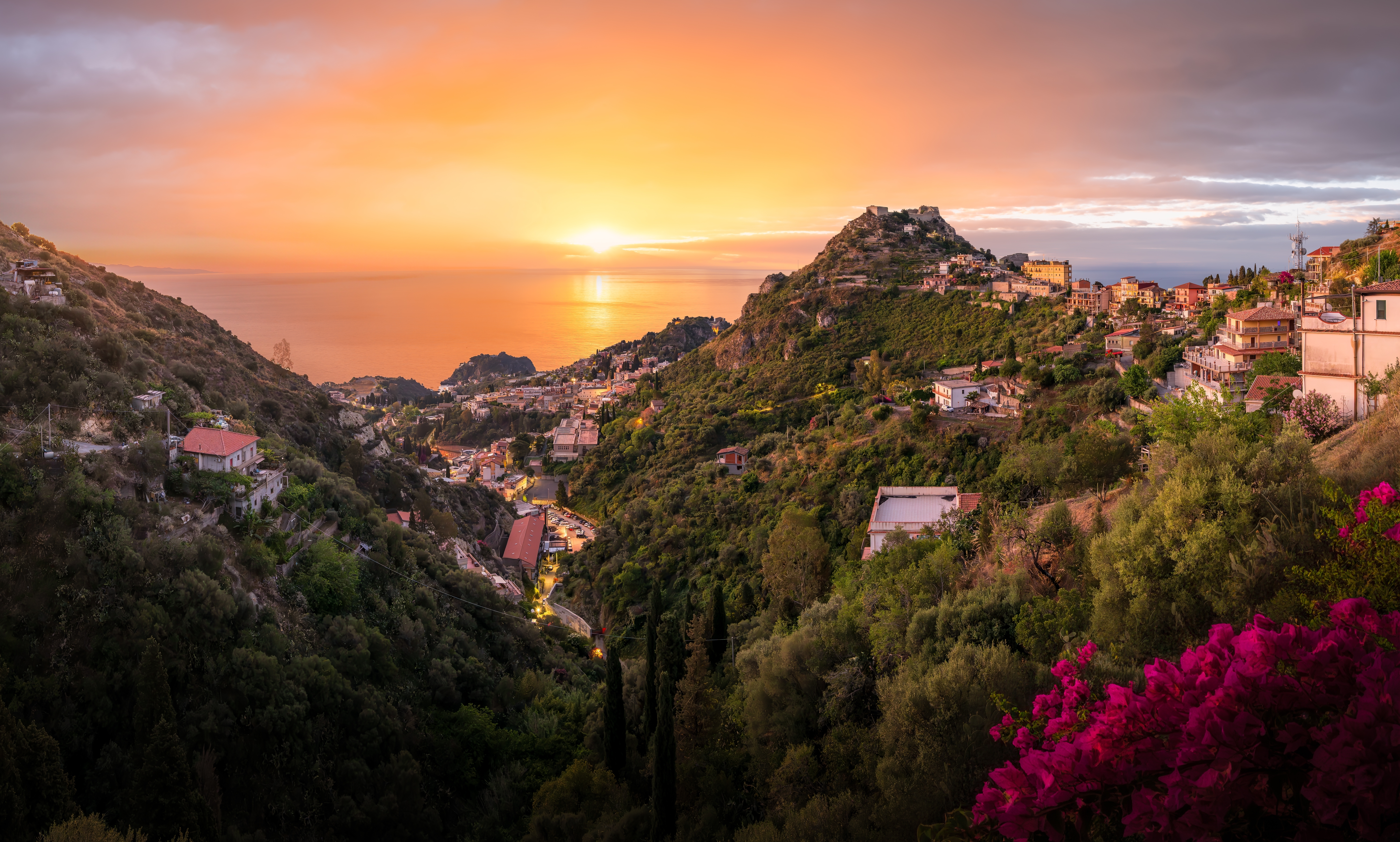 Magisk solnedgang over Taormina på Sicilien med gylden himmel, der oplyser den maleriske kystby på bjergskråningen med udsigt over Middelhavet