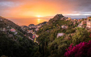 Magisk solnedgang over Taormina på Sicilien med gylden himmel, der oplyser den maleriske kystby på bjergskråningen med udsigt over Middelhavet
